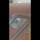 Emi hovers over a hospital toilet next to the grab bars and shits into the bowl, filmed from below. Vertical format video. Over 0.5 minutes.